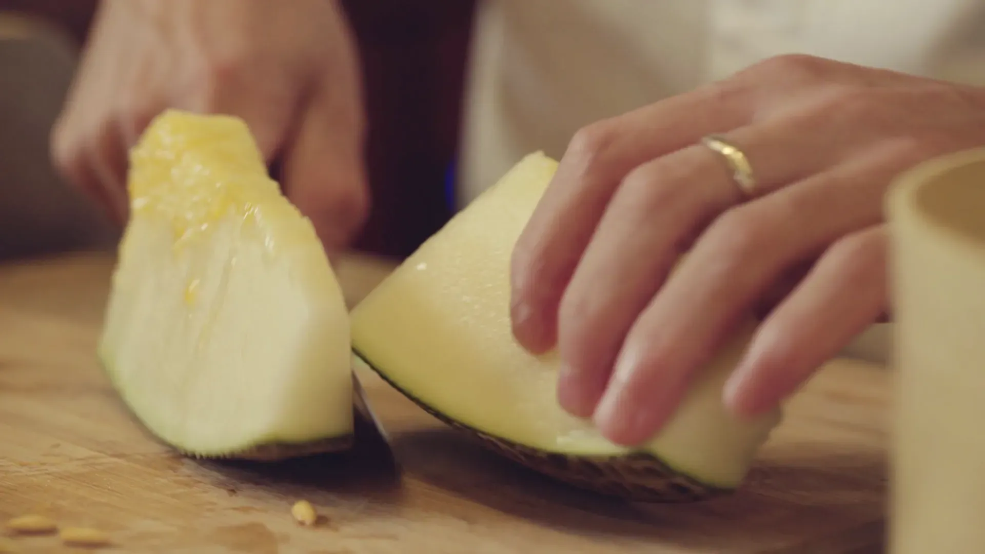 Fotograma del vídeo: unas manos cortan un trozo de melón sobre una tabla de madera