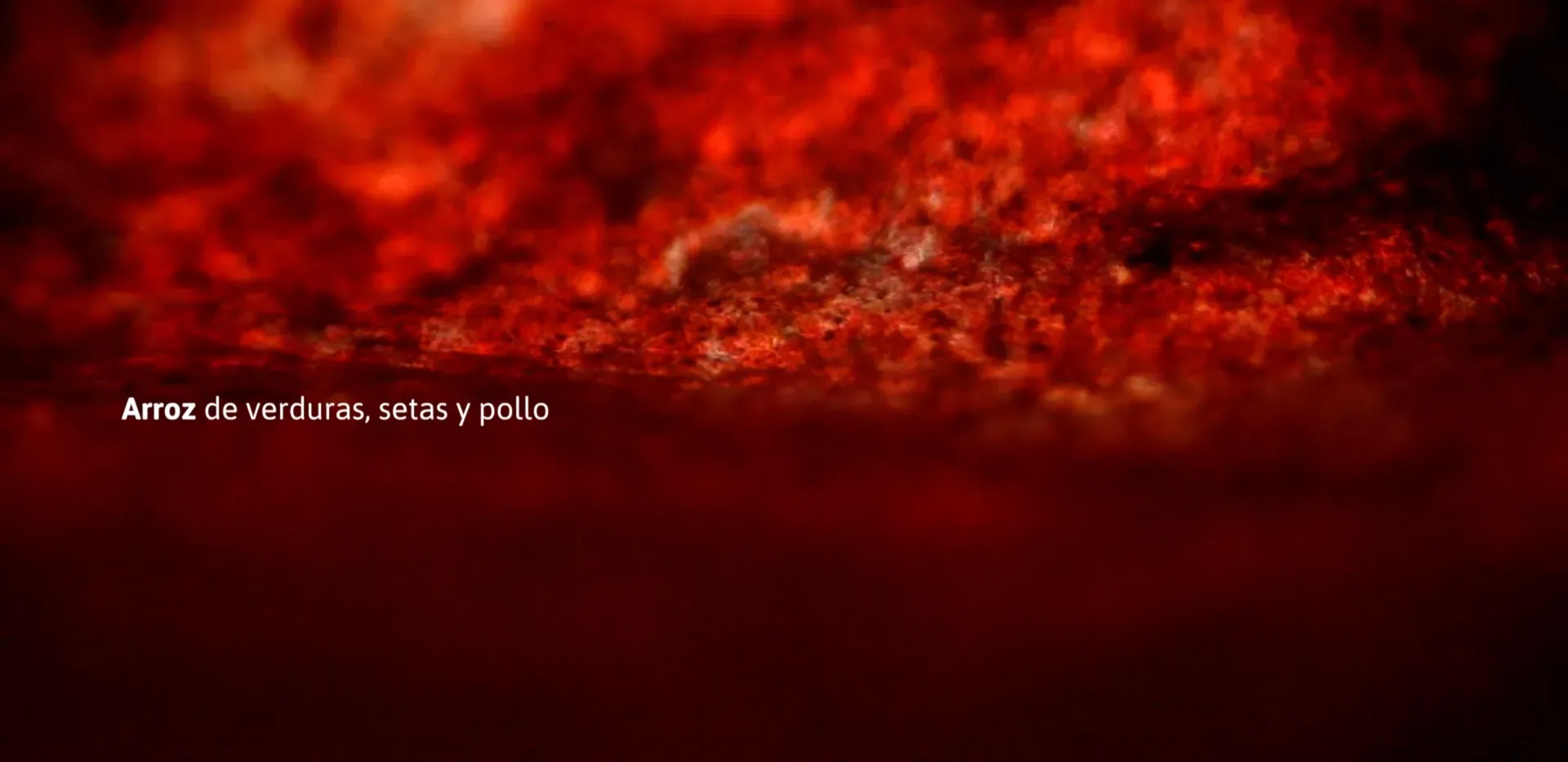 Fotograma del vídeo: plano macro de una textura roja desenfocada, con el rótulo «Arroz de verduras, setas y pollo»